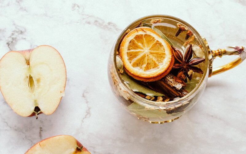 cravo-da-índia com limão — Flat lay of herbal tea with apple slices, dried lemon, and star anise on marble.