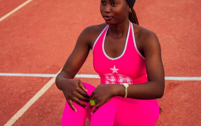 preparo emocional e físico no esporte — Young female athlete in pink sportswear sitting on a running track during the day.