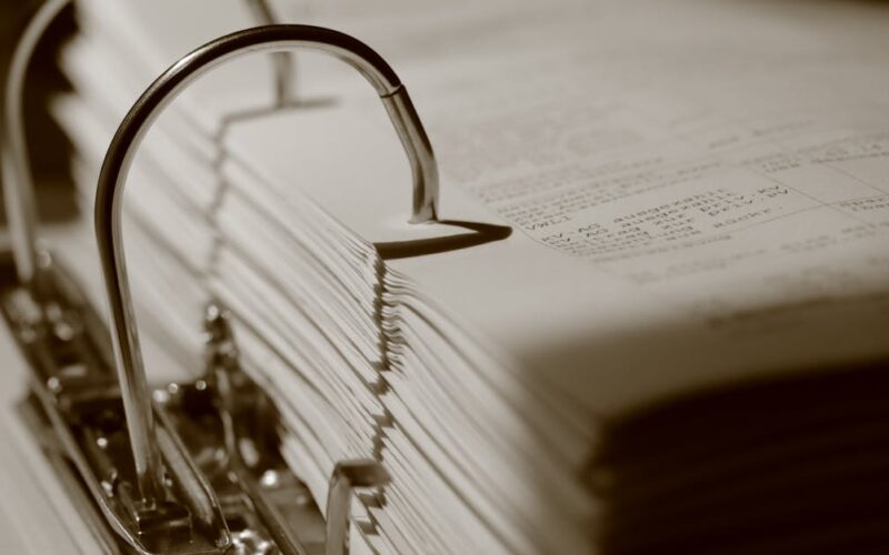 planejar documentação para emergências — Detailed sepia close-up of a binder filled with documents, emphasizing texture.