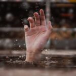 chuva intensa — A single hand emerges from water, symbolizing a cry for help amidst a rainy setting.
