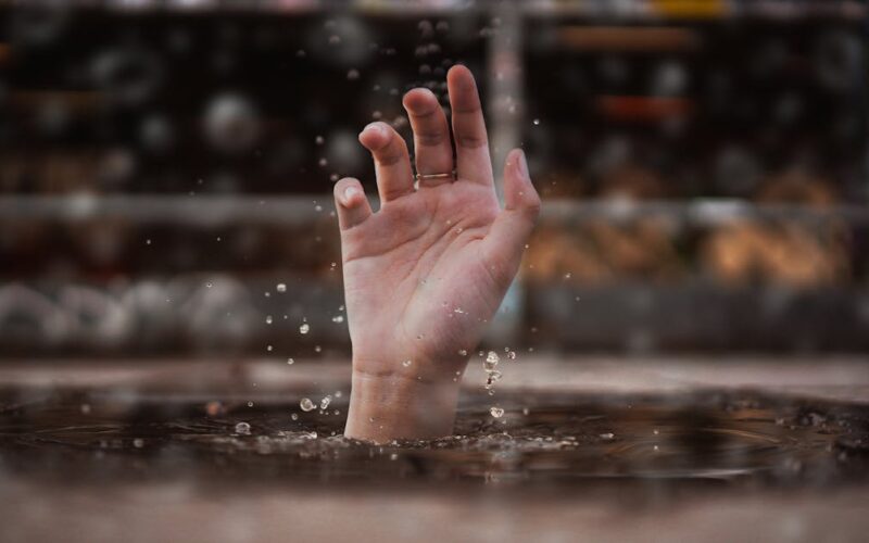 chuva intensa — A single hand emerges from water, symbolizing a cry for help amidst a rainy setting.
