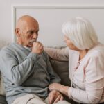 infecções respiratórias graves — An elderly woman comforts a man coughing on a couch, showcasing care and affection.