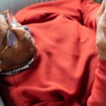 celulares para idosos — Senior man in red sweater using smartphone while lying on a sofa, enjoying leisure time indoors.