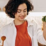 alimentação balanceada melhor idade — A woman in a kitchen preparing a fresh and healthy vegetable salad with cucumbers and cherry tomatoes.