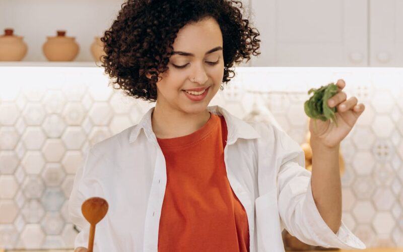 alimentação balanceada melhor idade — A woman in a kitchen preparing a fresh and healthy vegetable salad with cucumbers and cherry tomatoes.