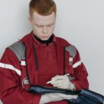 documentação essencial para emergências — A male paramedic in red uniform writing notes while sitting indoors, focused and professional.