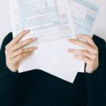 organizar documentos pessoais — A woman concealing her face with tax forms, illustrating financial stress and paperwork burden.