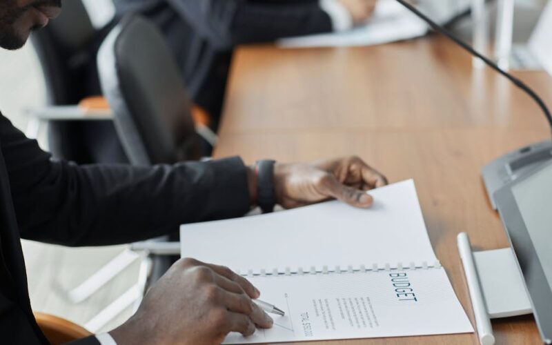 Super-PEC 2027 e IRPFM — Professional businessman examining budget documents during an office meeting, showcasing focus and analysis.