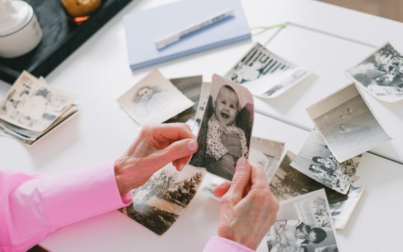 preservar memórias familiares — A person in a pink shirt organizing old black and white family photos on a table.