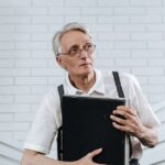 regra de transição penduricalhos aposentadoria — Elderly man in glasses and suspenders holding a briefcase in a modern office setting.
