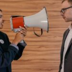 machismo nas interações públicas — A woman using a megaphone to confront a man in a suit indoors, symbolizing political debate.