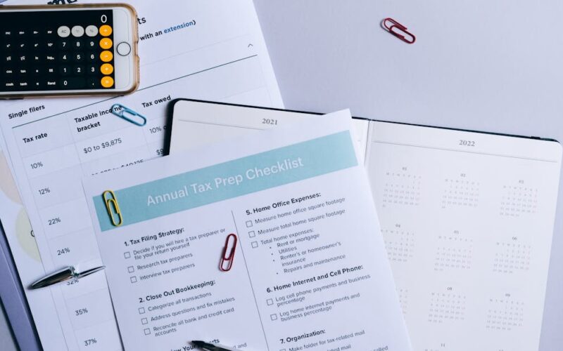 organizar documentos pessoais — Flat lay of a tax preparation checklist, calculator, and financial documents on a desk.