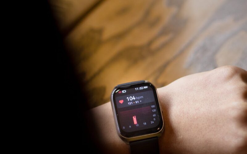 tecnologia vestível saúde desempenho — A close-up shot of a smartwatch on a wrist showing a heart rate of 104 bpm.