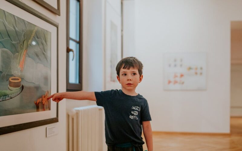 Visitar museus e exposições culturais — A young boy pointing at artwork in a modern art gallery, showing interest and curiosity.