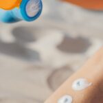 câncer de pele no couro cabeludo — Woman applying sunscreen lotion on leg at the beach. Summer skincare routine for sun protection outdoors.