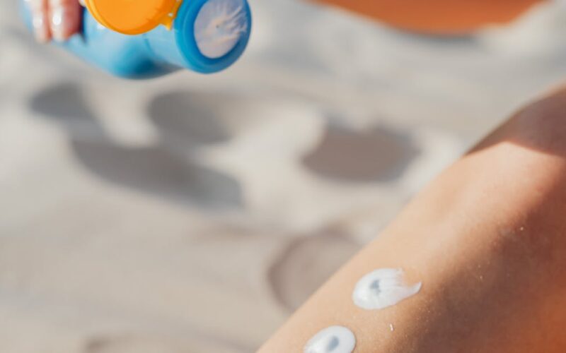 câncer de pele no couro cabeludo — Woman applying sunscreen lotion on leg at the beach. Summer skincare routine for sun protection outdoors.