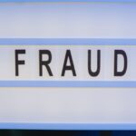 escândalo do INSS — Close-up of hands holding a sign with 'fraud', illuminated in blue light.