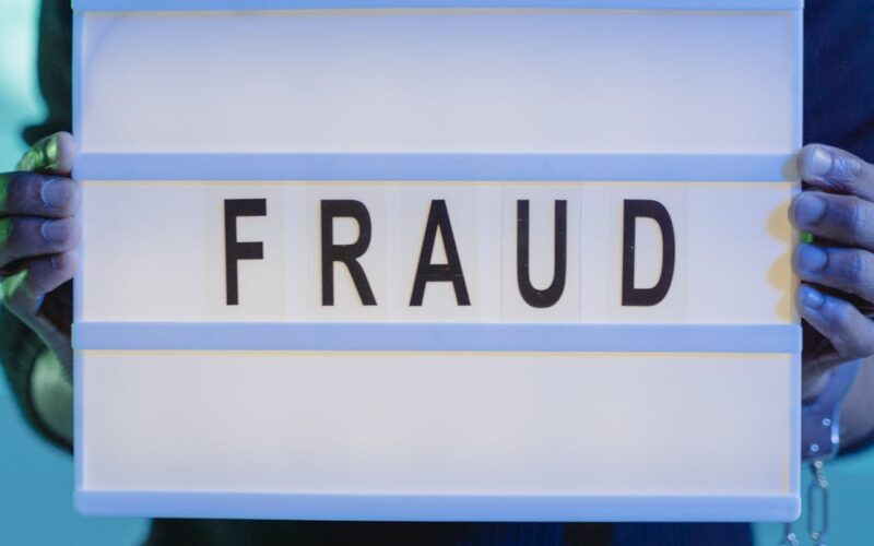 escândalo do INSS — Close-up of hands holding a sign with 'fraud', illuminated in blue light.