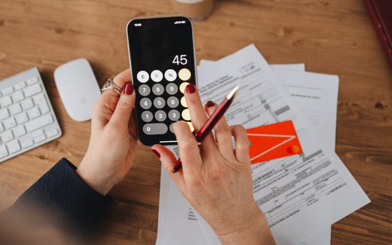 desconto pagamento antecipado IPVA — Hands using a calculator app on a smartphone over financial documents. Perfect for illustrating finance or technology themes.