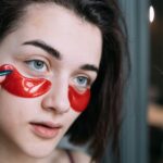conjuntivite prevenção tratamento — Young woman applying vibrant red under eye patches for skincare.