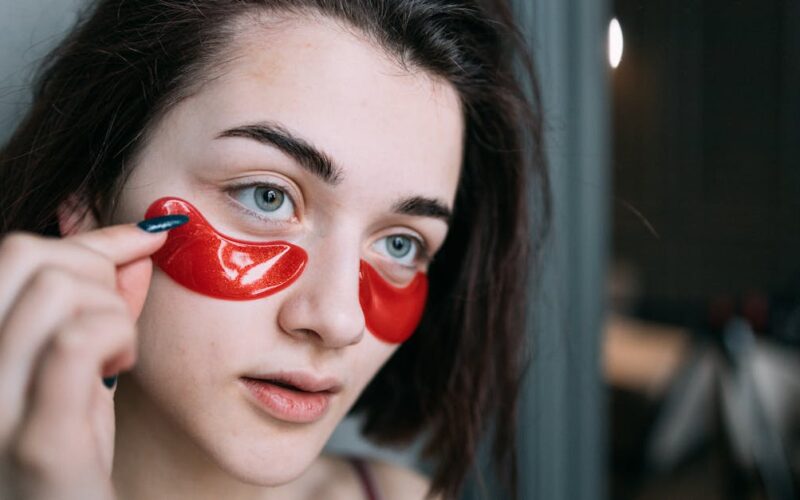 conjuntivite prevenção tratamento — Young woman applying vibrant red under eye patches for skincare.