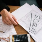 venda parcelada imóvel IR 2026 — Hands of a person examining tax forms labeled as scam with calculator and papers.