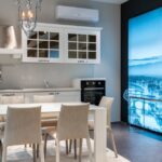 uso eficiente do ar-condicionado — White dining table with soft chairs placed in spacious kitchen with elegant furniture and chandelier in modern studio apartment