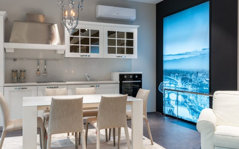 uso eficiente do ar-condicionado — White dining table with soft chairs placed in spacious kitchen with elegant furniture and chandelier in modern studio apartment