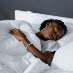 qualidade do sono na maturidade — A man sleeping peacefully under a white blanket in a cozy bedroom.