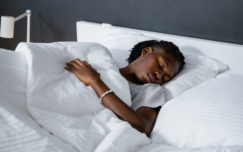 qualidade do sono na maturidade — A man sleeping peacefully under a white blanket in a cozy bedroom.