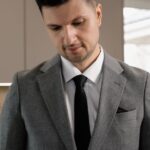 venda parcelada imóvel IR — Male real estate agent in suit reviewing property documents indoors.