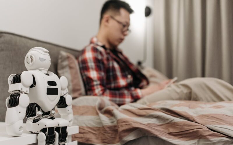 inteligência artificial ética — A modern bedroom featuring a robot on a bedside table and a man sitting on a bed.