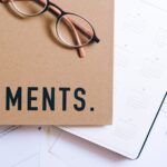 documentação pessoal para emergências — Flat lay of office supplies including documents, calendar, and eyeglasses on a desk.