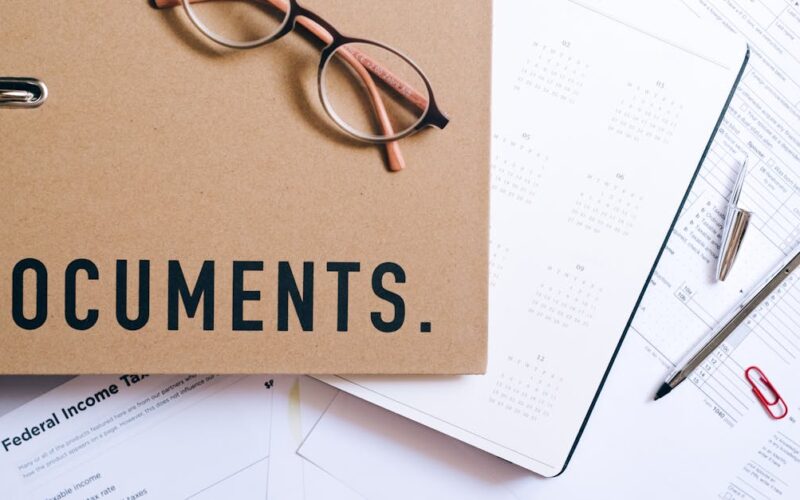 documentação pessoal para emergências — Flat lay of office supplies including documents, calendar, and eyeglasses on a desk.