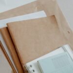 organizar documentos pessoais — Woven basket filled with notebooks, papers, and office supplies on a wooden desk.