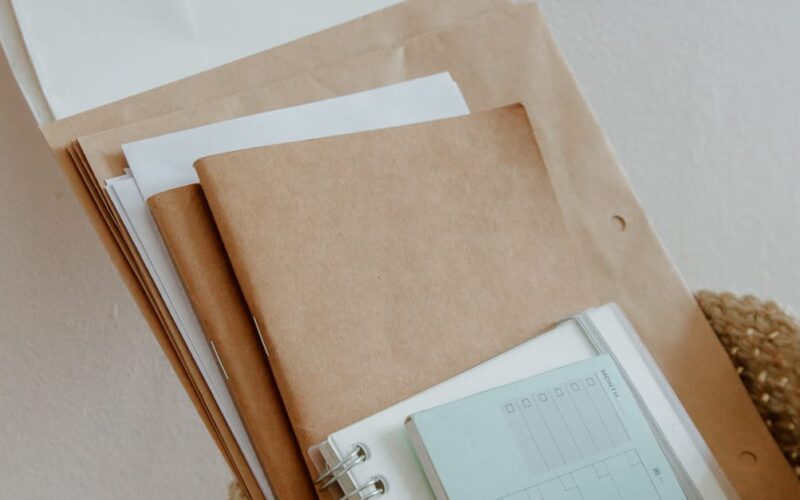 organizar documentos pessoais — Woven basket filled with notebooks, papers, and office supplies on a wooden desk.