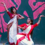 C6 Fest 2026 artistas e novidades — Two women in traditional saris perform a dance against a vibrant graffiti wall in Dhaka, Bangladesh.