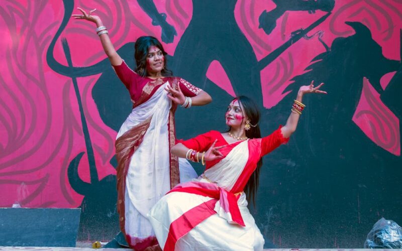 C6 Fest 2026 artistas e novidades — Two women in traditional saris perform a dance against a vibrant graffiti wall in Dhaka, Bangladesh.