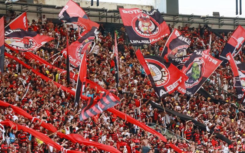 Uniformes históricos do Flamengo 2027 — A lively crowd of Flamengo supporters waving flags at Maracanã Stadium in Rio de Janeiro.