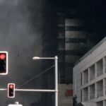 interdição de imóveis após explosões — A dramatic scene of a high-rise fire in Dubai Marina with thick smoke and traffic lights.