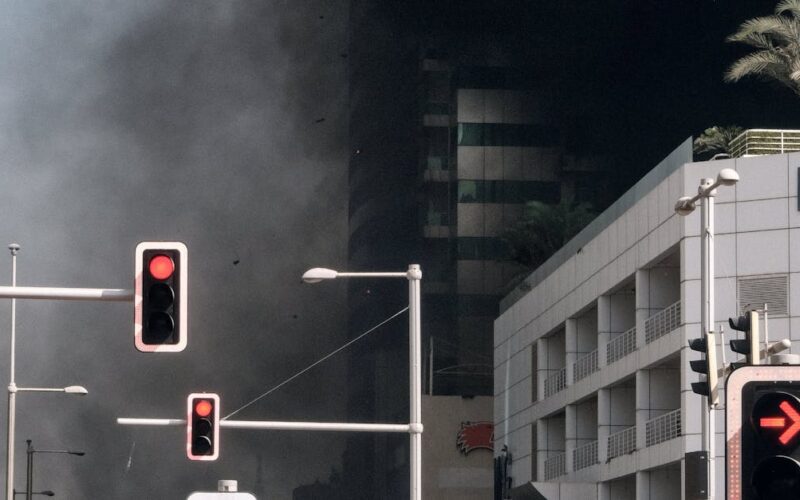 interdição de imóveis após explosões — A dramatic scene of a high-rise fire in Dubai Marina with thick smoke and traffic lights.