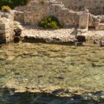 cidade submersa sul de minas — Ancient ruins partially submerged in clear coastal waters surrounded by lush greenery.