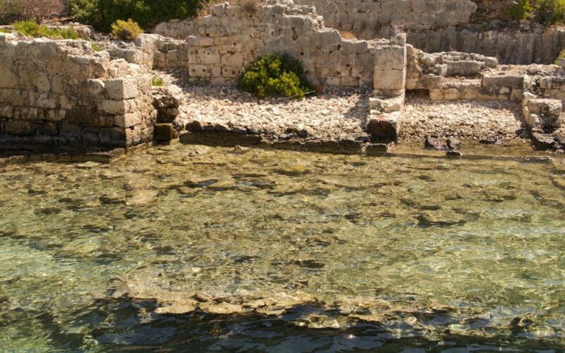 cidade submersa sul de minas — Ancient ruins partially submerged in clear coastal waters surrounded by lush greenery.