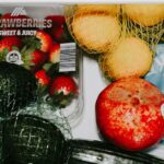 conservar frutas e legumes — A variety of fresh fruits and vegetables including avocados, lemons, strawberries, and lettuce in a fridge drawer.