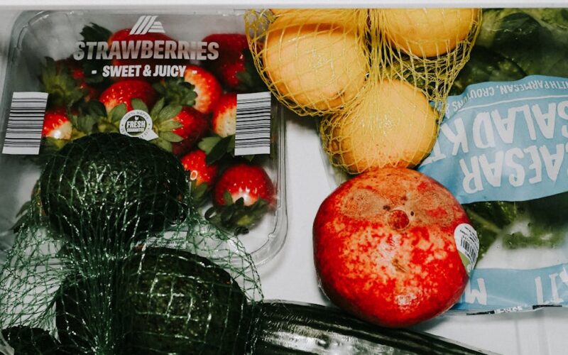 conservar frutas e legumes — A variety of fresh fruits and vegetables including avocados, lemons, strawberries, and lettuce in a fridge drawer.
