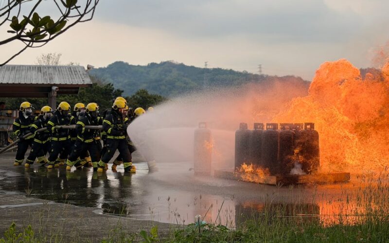 investimentos segurança civil bombeiros — Team of firefighters using hoses to extinguish a controlled outdoor blaze during training.
