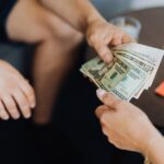 quinto dia útil — Close-up of hands exchanging US dollar bills, symbolizing a financial transaction or payment.