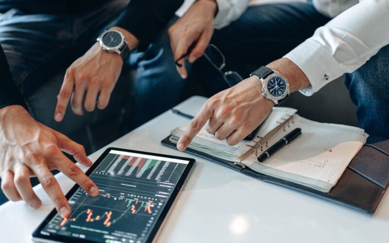 resultados econômicos para investidores — Two businessmen discussing financial data on a tablet during a meeting.