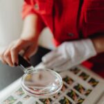 pirataria e fraudes financeiras — A person closely examines postage stamps with a magnifying glass, revealing intricate details.