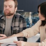 restituição imposto de renda falecido — A couple looks worried as they review bills at their kitchen table, reflecting financial concerns.
